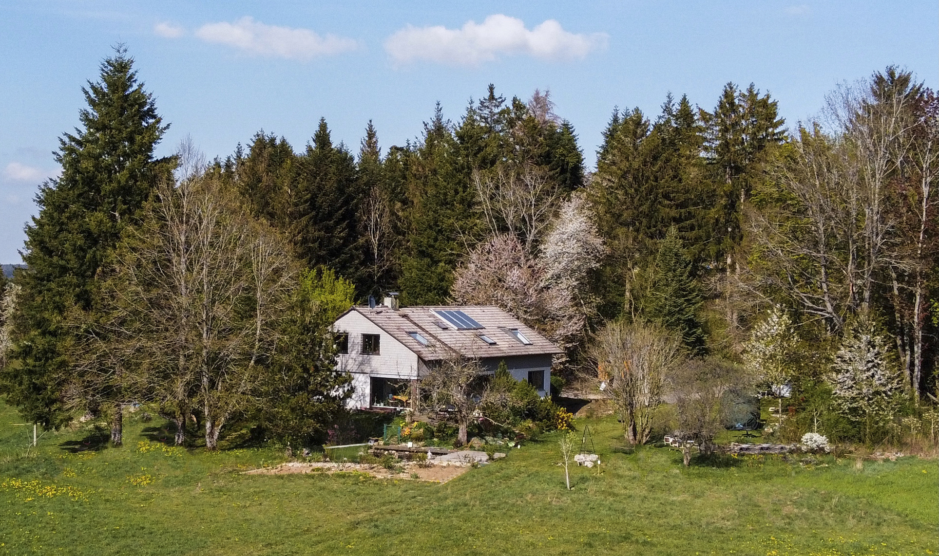 Großaufnahme des zweistöckigen Waldhauses, mit Gartenanlage im Vordergund und Waldbereich im Hintergrund